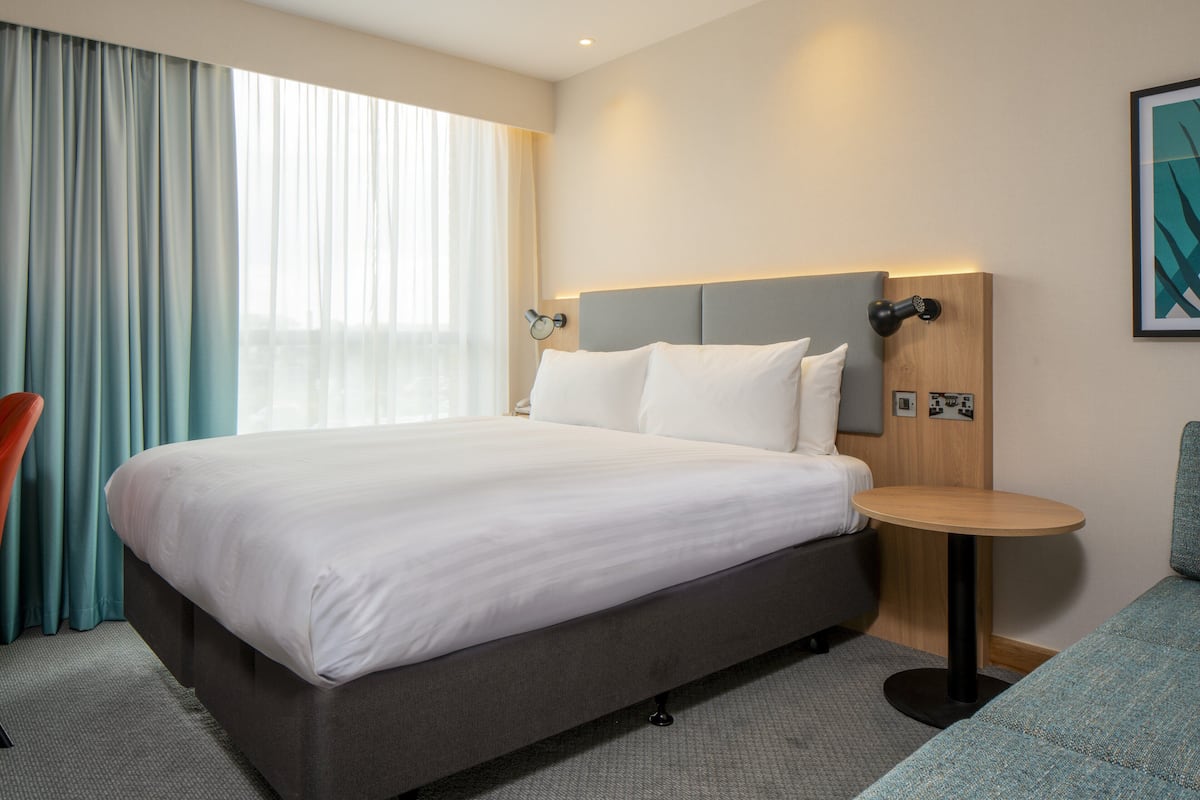 A hotel room with a large bed, a round table, a sofa, and a view of the city through the window.