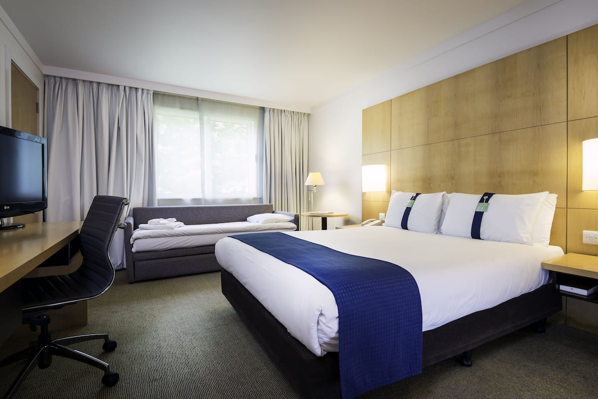 A hotel room with a bed, a desk, a chair, a TV, and a window with curtains.
