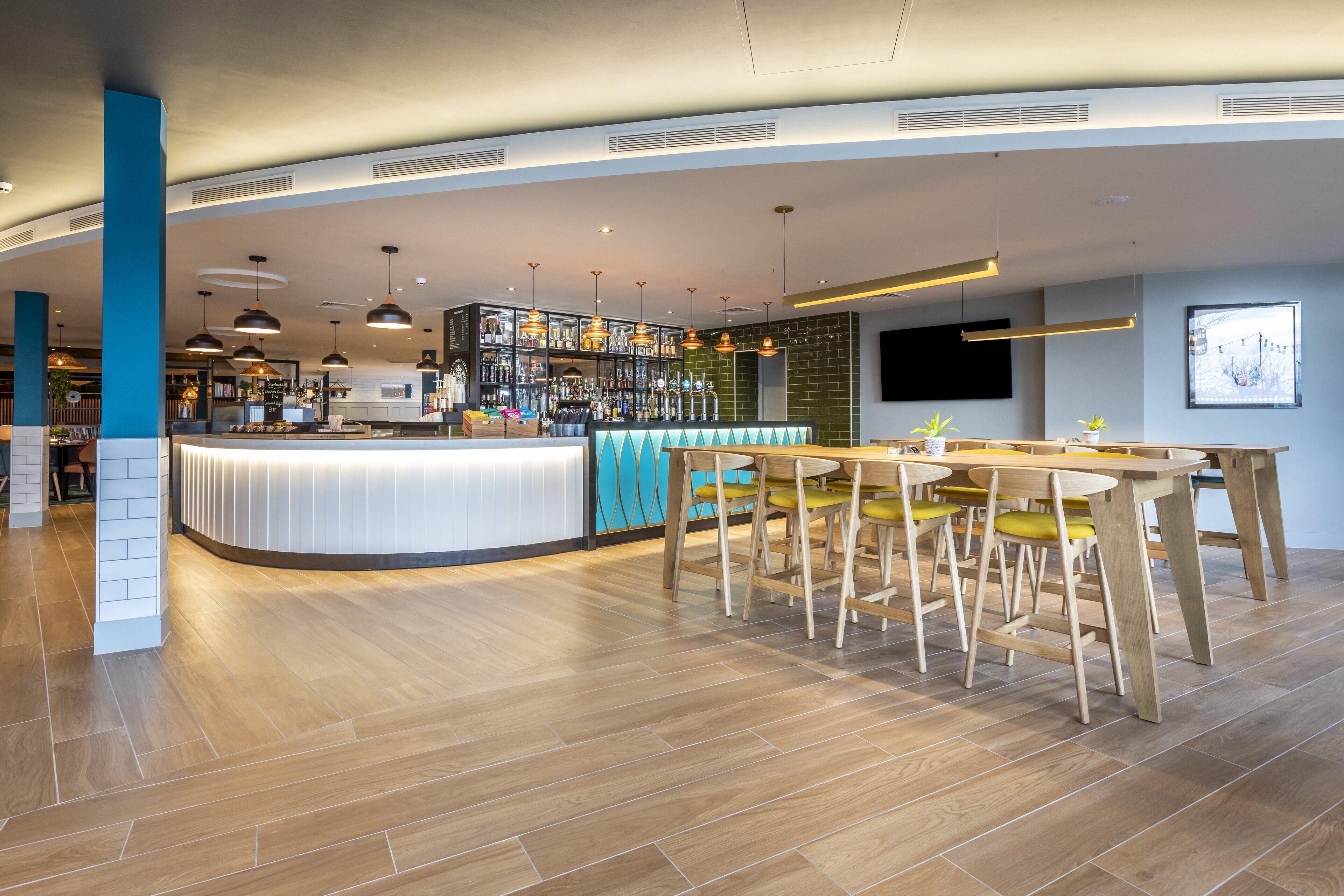 A modern bar area with a curved counter, wooden chairs, and pendant lighting.