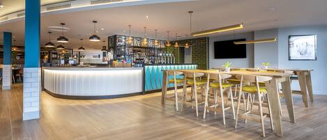 A modern bar area with a curved counter, wooden chairs, and pendant lighting.