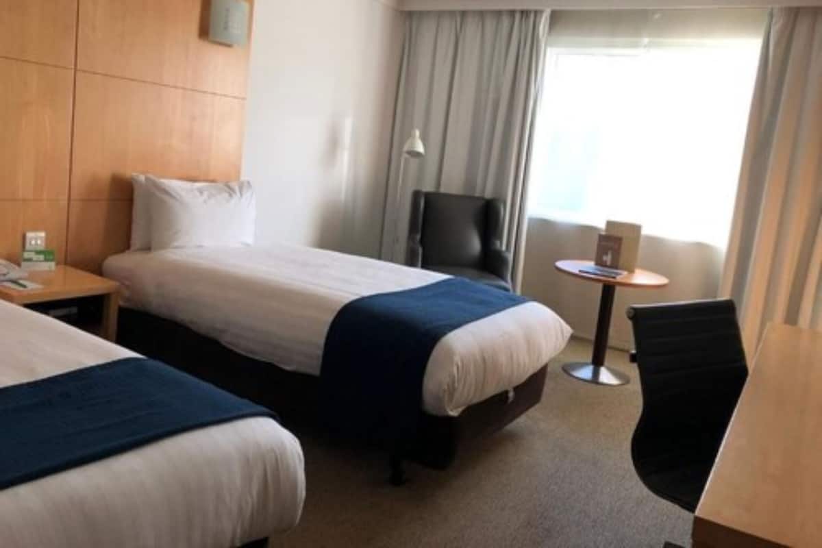 A hotel room with two beds, a desk, a chair, a lamp, and a window with curtains.