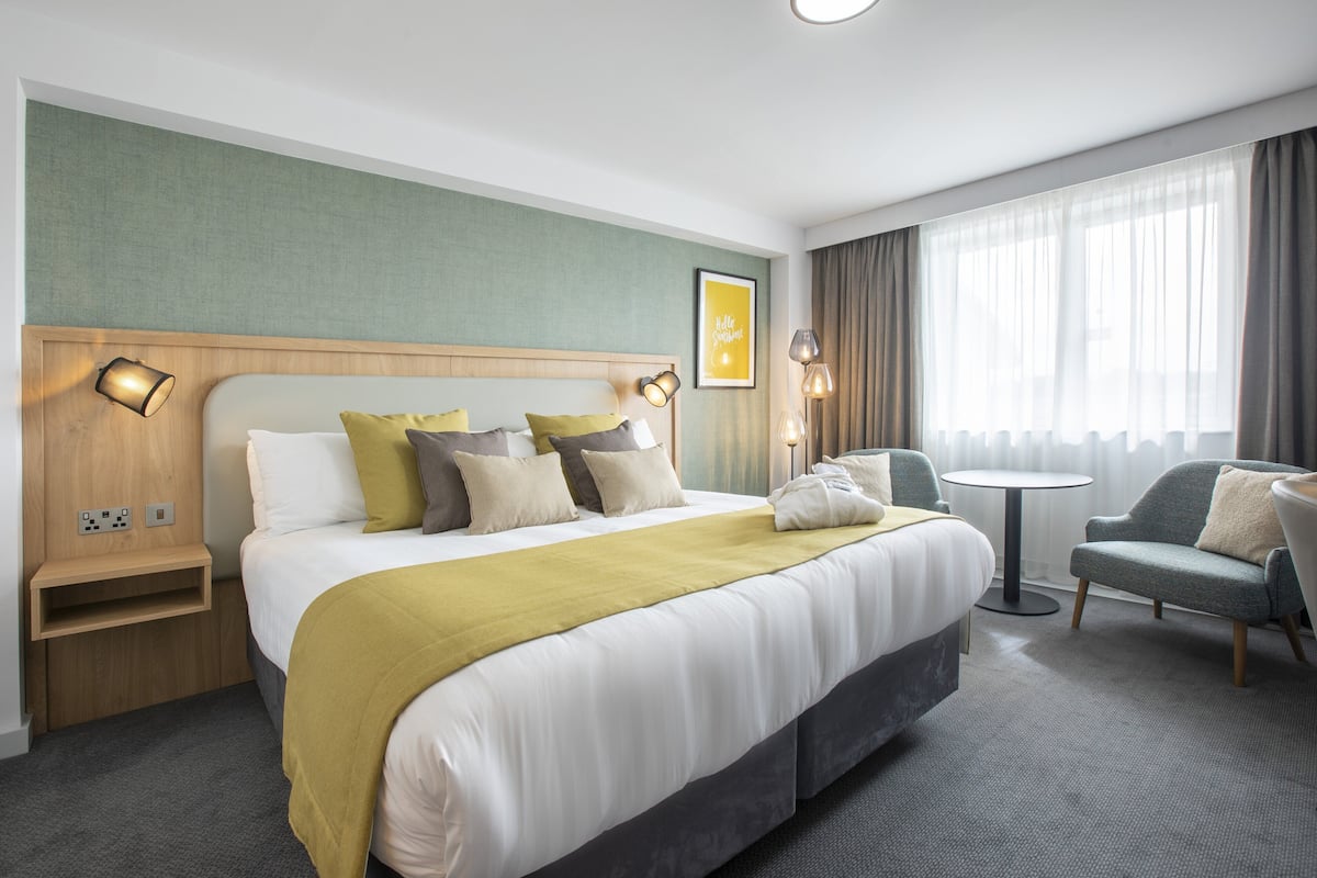 A hotel room with a large bed, bedside tables, a small round table, and a sofa.