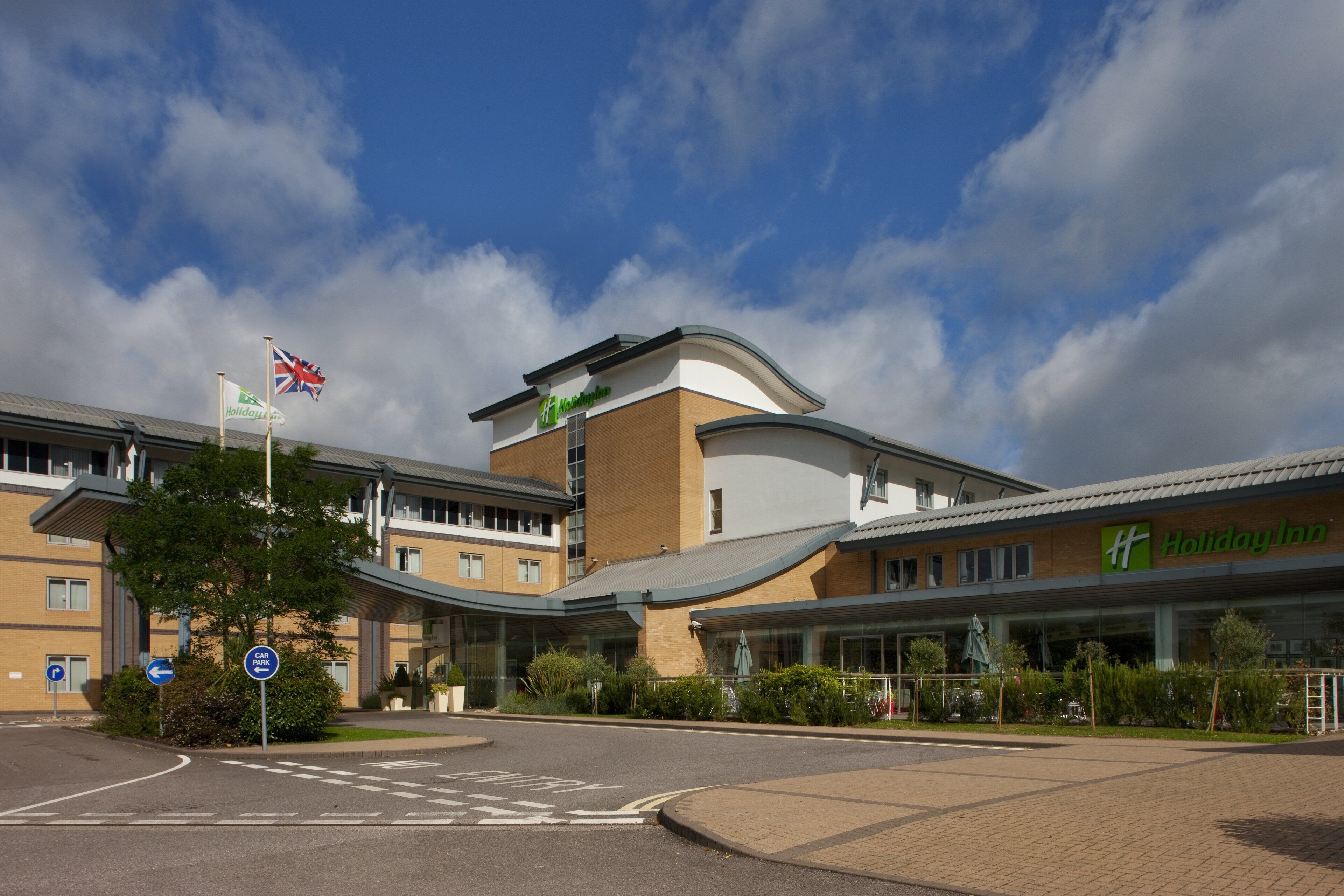 A Holiday Inn hotel with a curved facade, a car park sign, and a British flag.