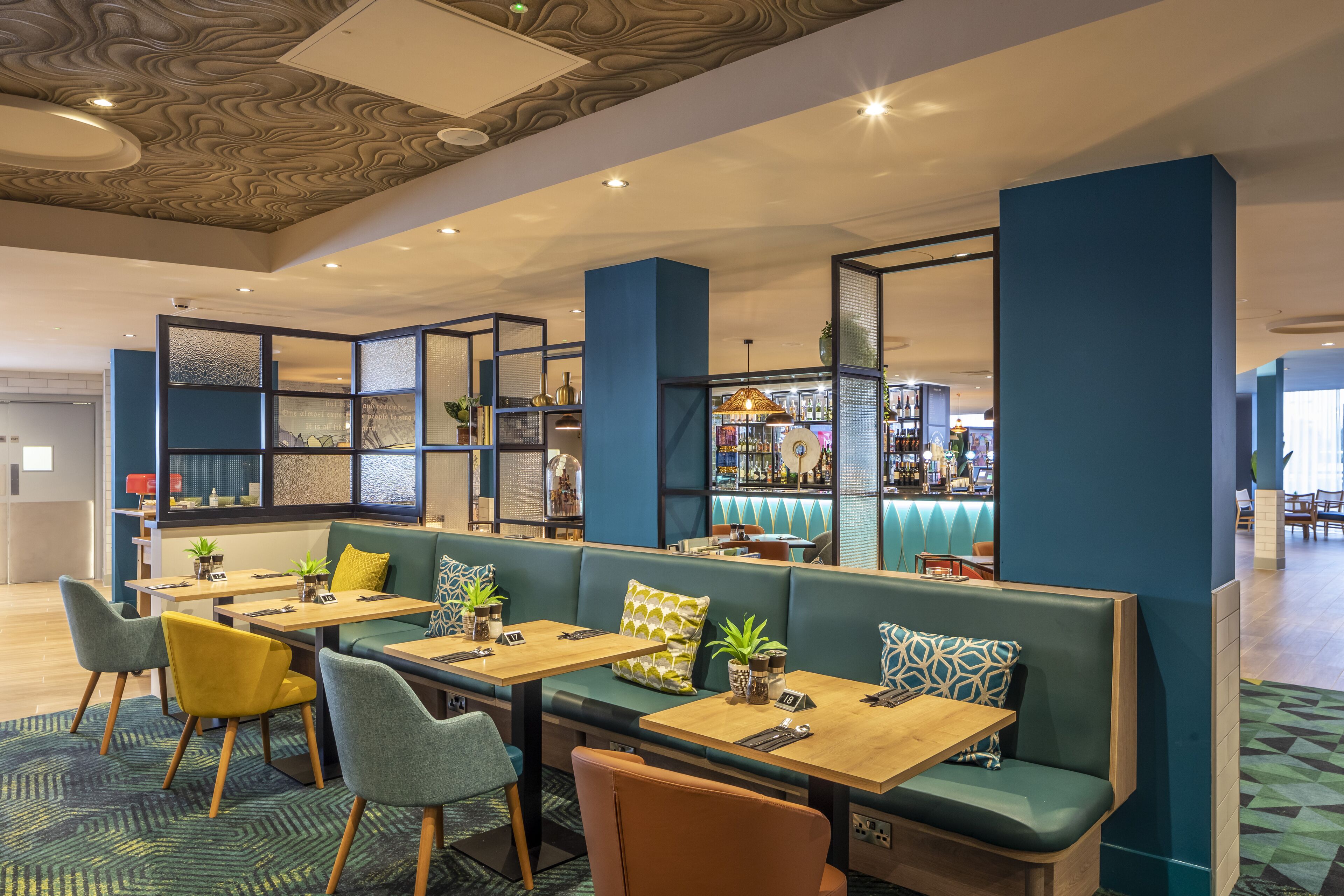 A modern restaurant with booths and tables, a bar area, and decorative elements on the ceiling.