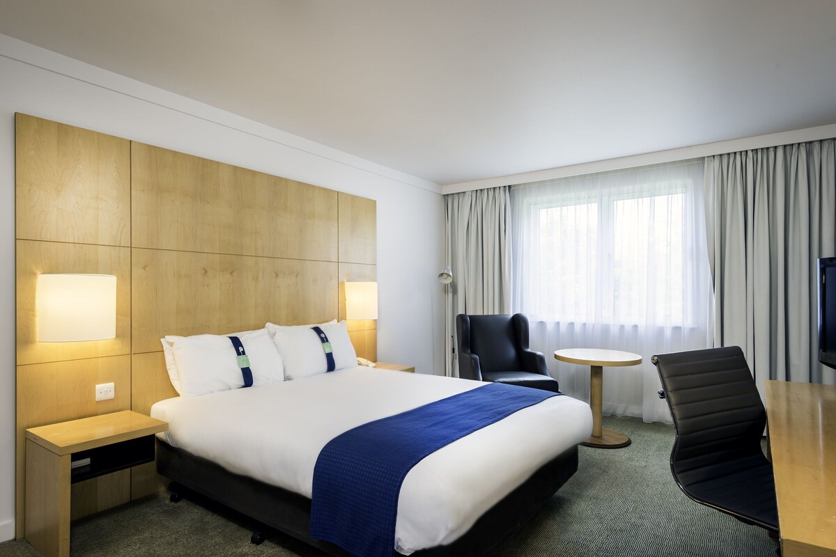 Habitación de hotel con una cama grande, mesitas de noche, un escritorio, una silla y una ventana con cortinas.