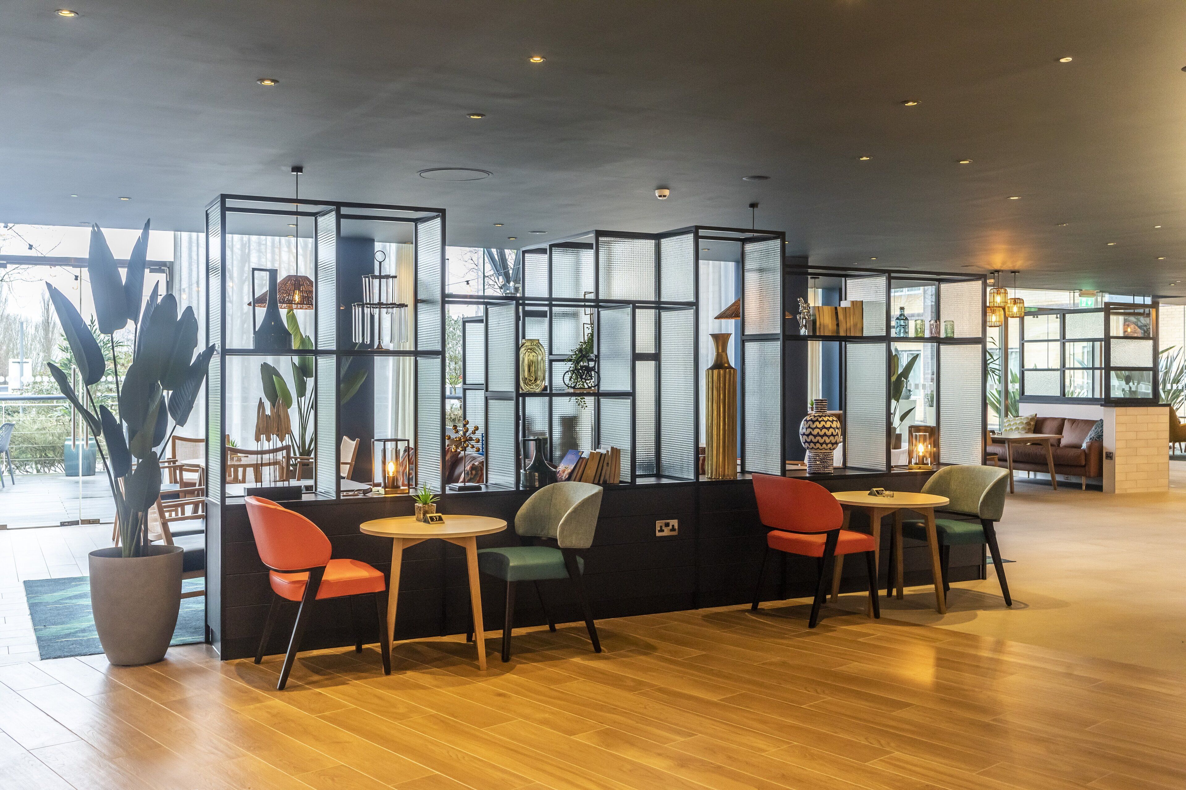 Een modern interieur met een zithoek, voorzien van een glazen scheiding, houten vloer en diverse decoratieve elementen.