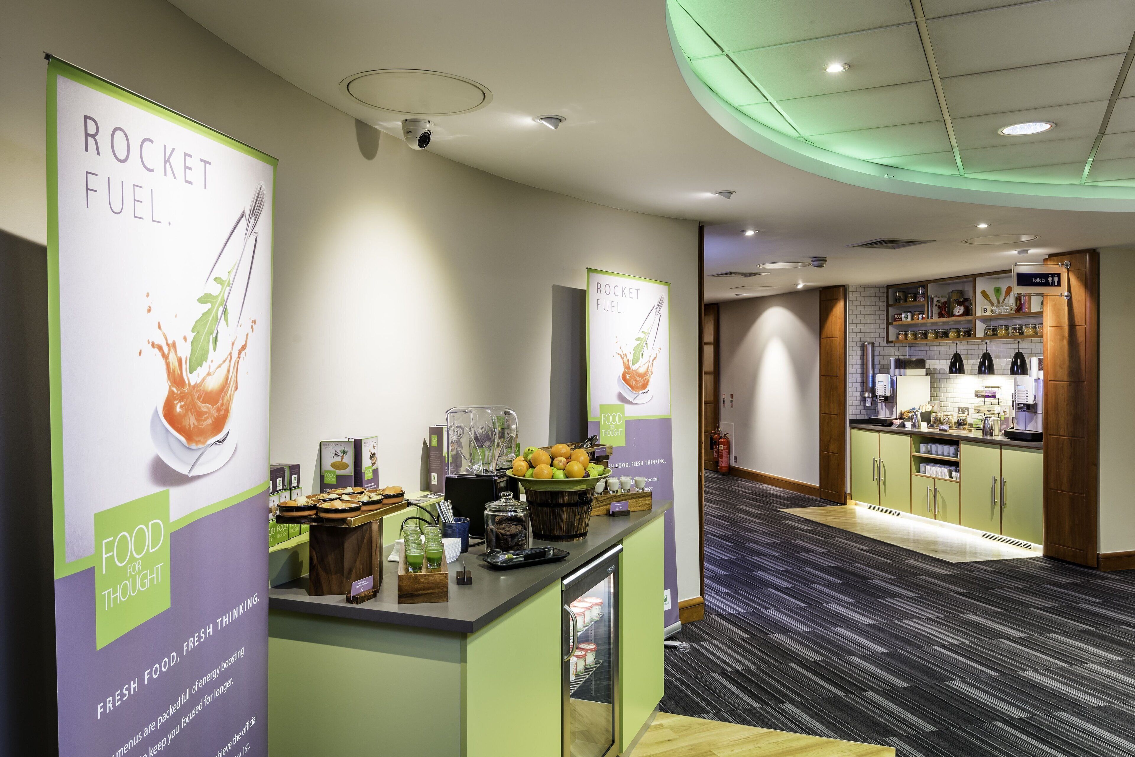 A modern kitchen area with a counter displaying food items and a sign promoting 'ROCKET FUEL'.
