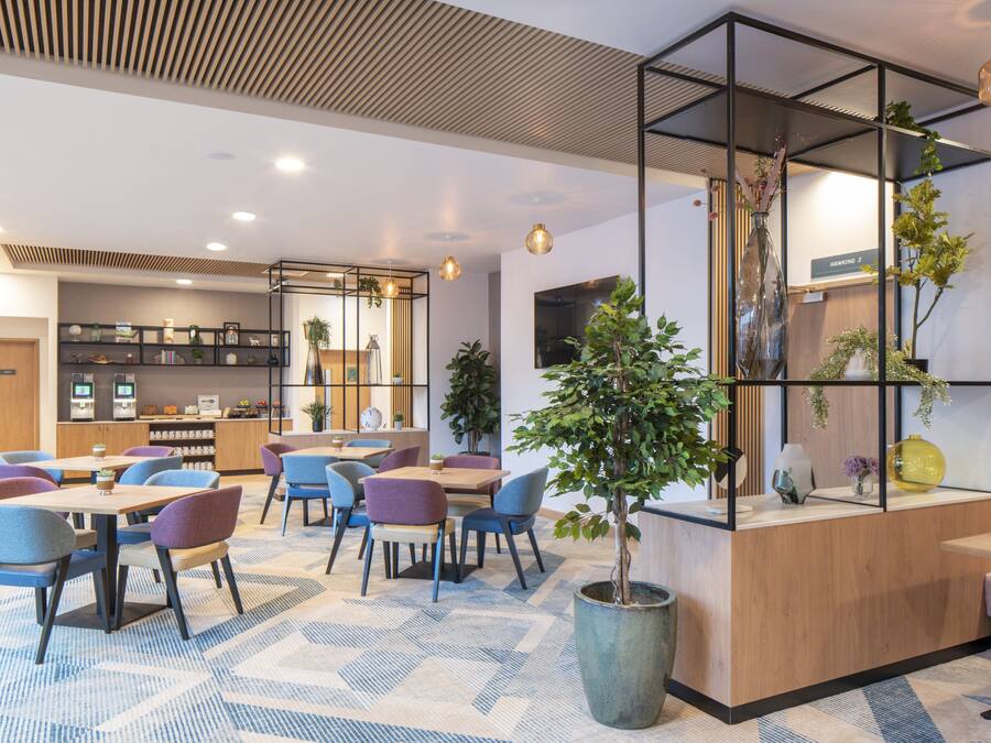 Un moderno hall de hotel con zona de estar, mostrador de recepción y barra de café.
