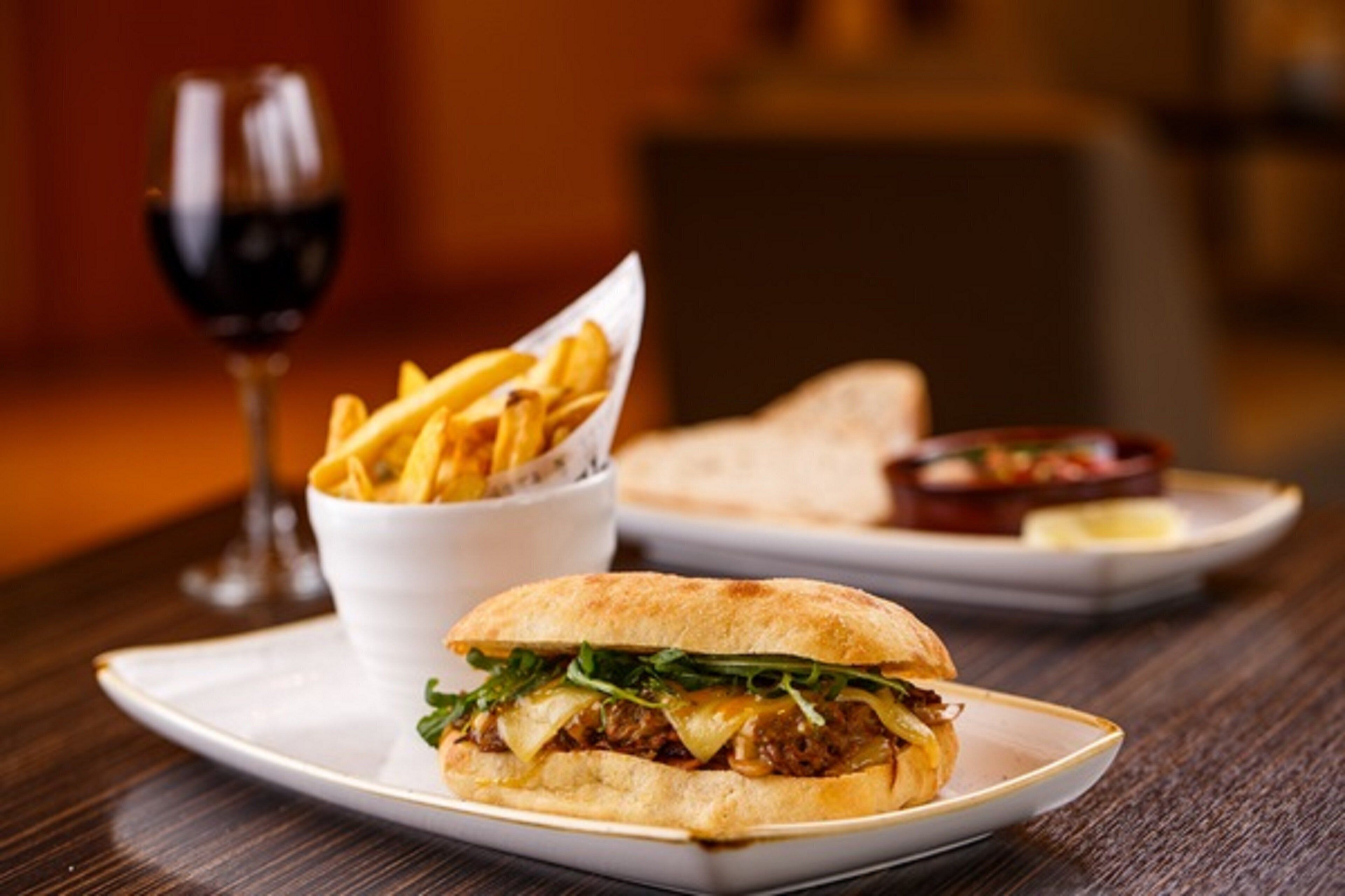 A sandwich on a plate with fries and a glass of red wine.