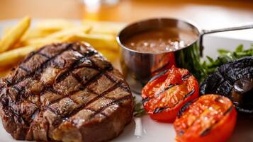 A steak with grill marks, French fries, grilled tomatoes, and a side of greens.