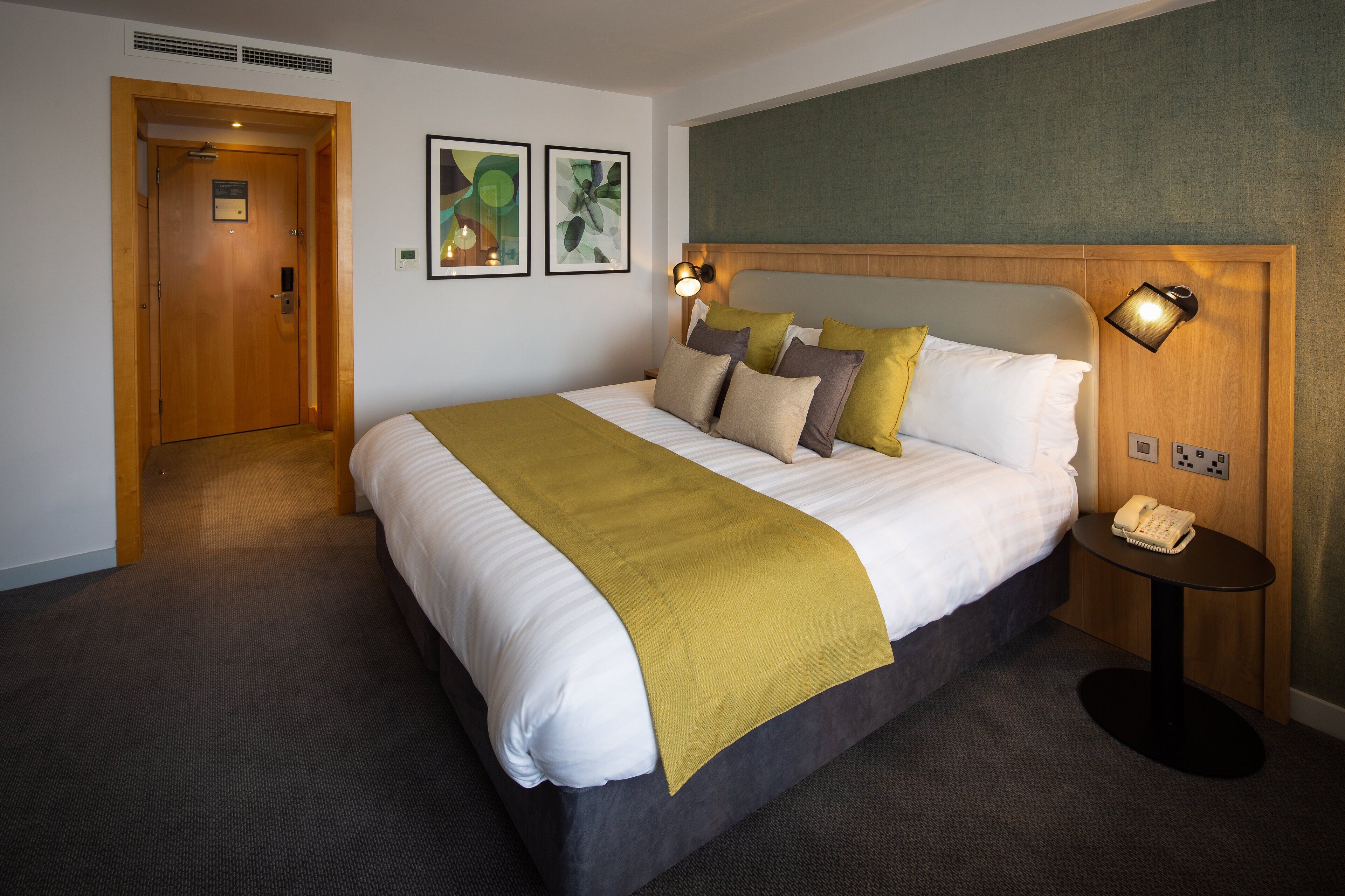 A hotel room with a large bed, a bedside table with a telephone, and a door leading to another room.