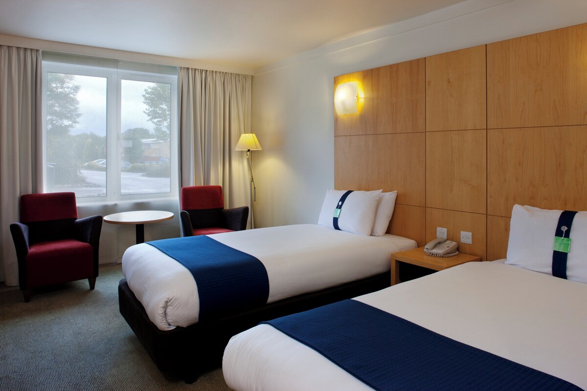 Habitación de hotel con dos camas, un escritorio, una silla y una ventana con cortinas.