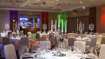 Un salón de banquetes con mesas redondas dispuestas para el servicio de comidas, cada una con mantel blanco, cubertería y copas de vino.