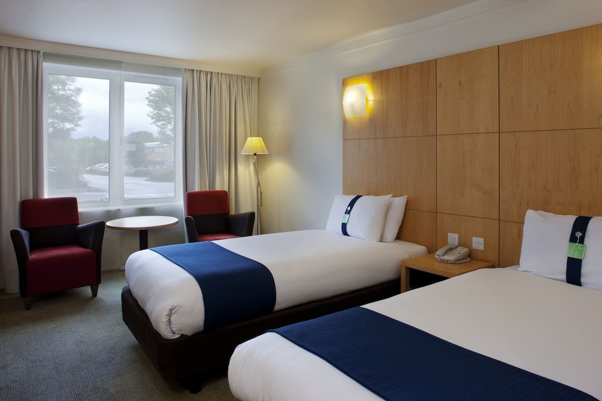 A hotel room with two beds, a desk, a chair, and a window with curtains.