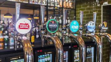 Fila de grifos de cerveza con etiquetas que incluyen Stella Artois, Beck's, Mellow, Revell y Guinness.