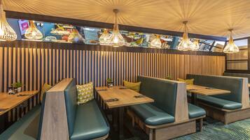 A restaurant with booth seating, wooden tables, and hanging pendant lights.