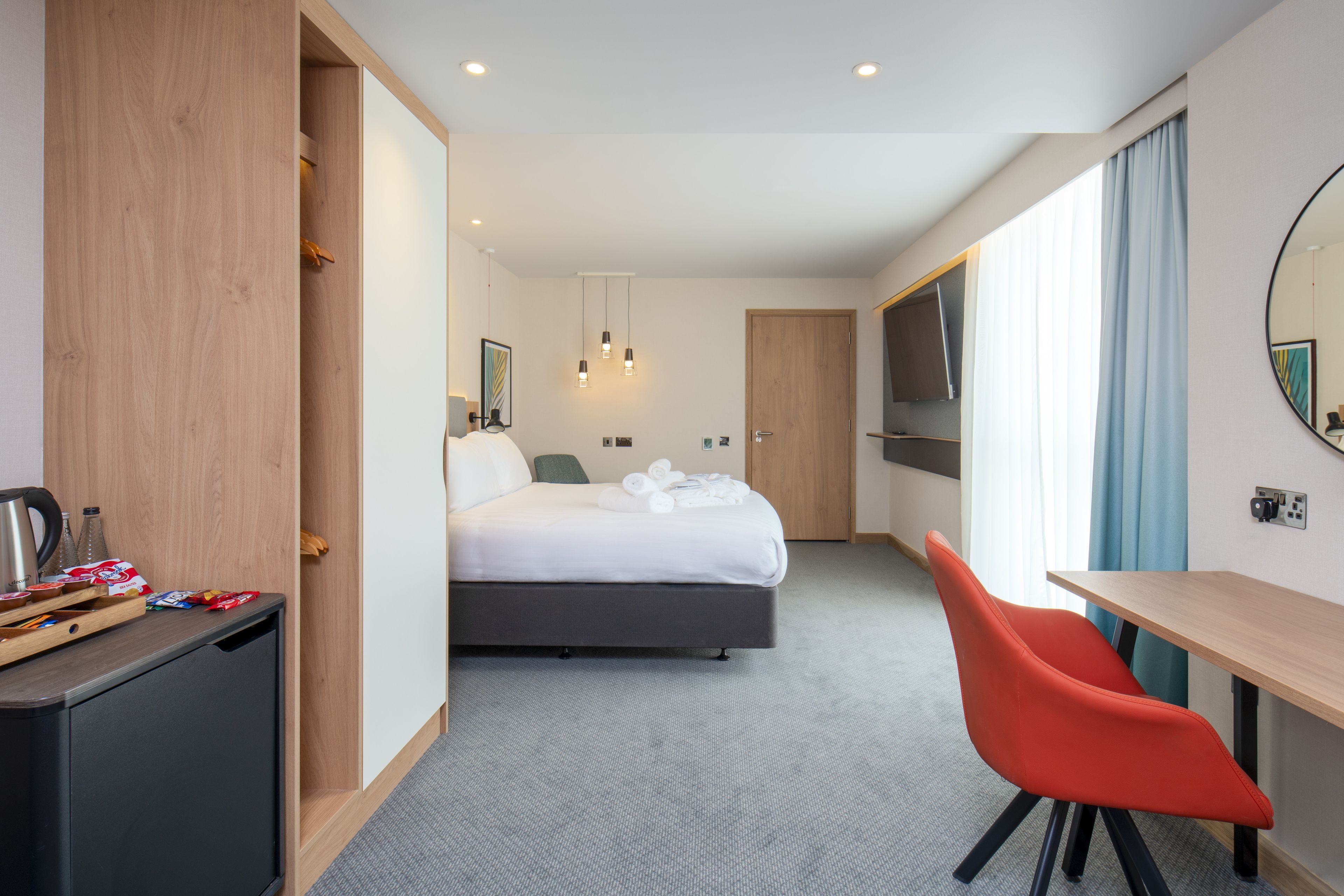 A hotel room with a bed, a desk, a chair, a TV, and a minibar.