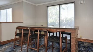 A hotel room with a bar area, three wooden bar stools, a large window, and a patterned carpet. - Fairfield by Marriott Inn & Suites Columbia Harbison (Columbia)