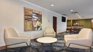 A hotel lobby with a round table, two armchairs, a large painting, a bar area, and a television on the wall. - Fairfield by Marriott Inn & Suites Columbia Harbison (Columbia)