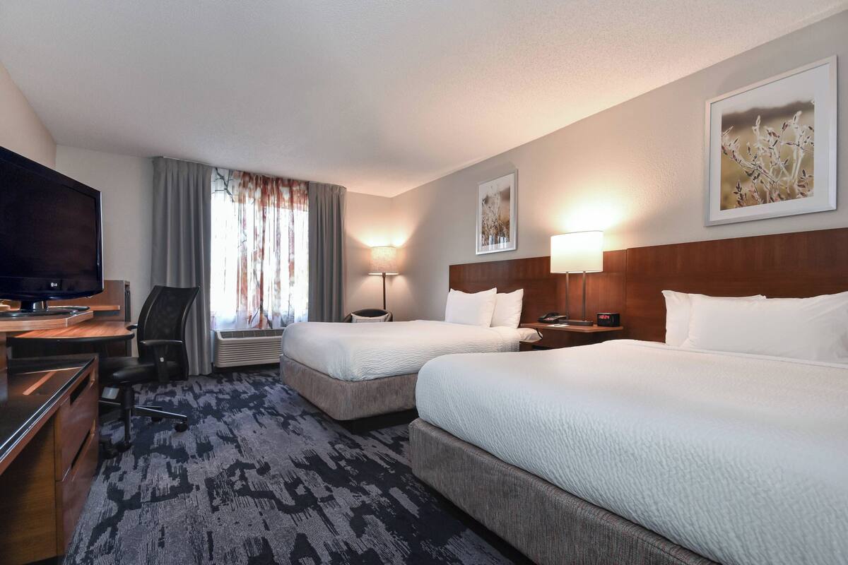 A hotel room with two beds, a desk, a TV, and a lamp.