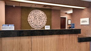 A hotel reception desk with a wooden panel design, a large decorative wall piece, and signs for 'Marriott Bonvoy' and 'Boundless'. - Fairfield by Marriott Inn & Suites Columbia Harbison (Columbia)