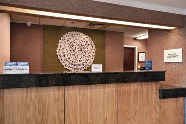 A hotel reception desk with a wooden panel design, a large decorative wall piece, and signs for 'Marriott Bonvoy' and 'Boundless'. - Fairfield by Marriott Inn & Suites Columbia Harbison (Columbia)