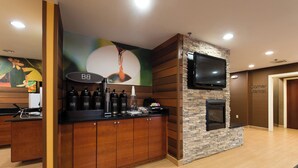 A modern bar area with a stone fireplace, a flat-screen TV, and a coffee station. - Fairfield Inn by Marriott Orangeburg (Orangeburg)
