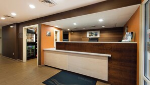 A reception area with a wooden reception desk, a welcome mat, a vending machine, and a clock on the wall. - Fairfield Inn by Marriott Orangeburg (Orangeburg)