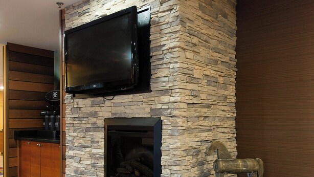 A stone fireplace with a television mounted above it, a small statue on the mantel, and a wooden cabinet to the left. - Fairfield Inn by Marriott Orangeburg (Orangeburg)