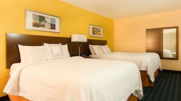 A hotel room with two beds, a wooden headboard, a nightstand, a lamp, and two framed pictures on the wall.