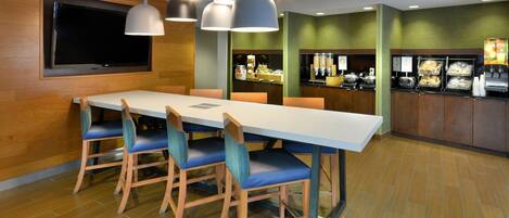 A conference room with a long table, blue chairs, and a flat-screen TV mounted on the wall.
