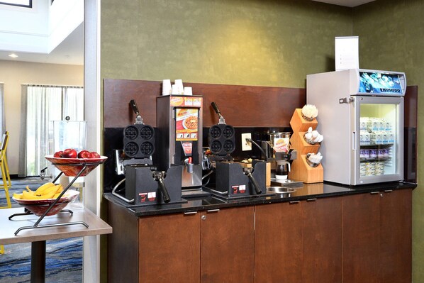 Una estación autoservicio para bebidas con una máquina de café, un dispensador de bebidas y un refrigerador.