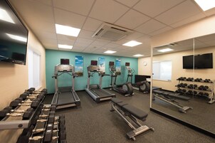 Ein Fitnessstudio mit Laufbändern, Crosstrainern, einer Hantelbank und Kurzhanteln.