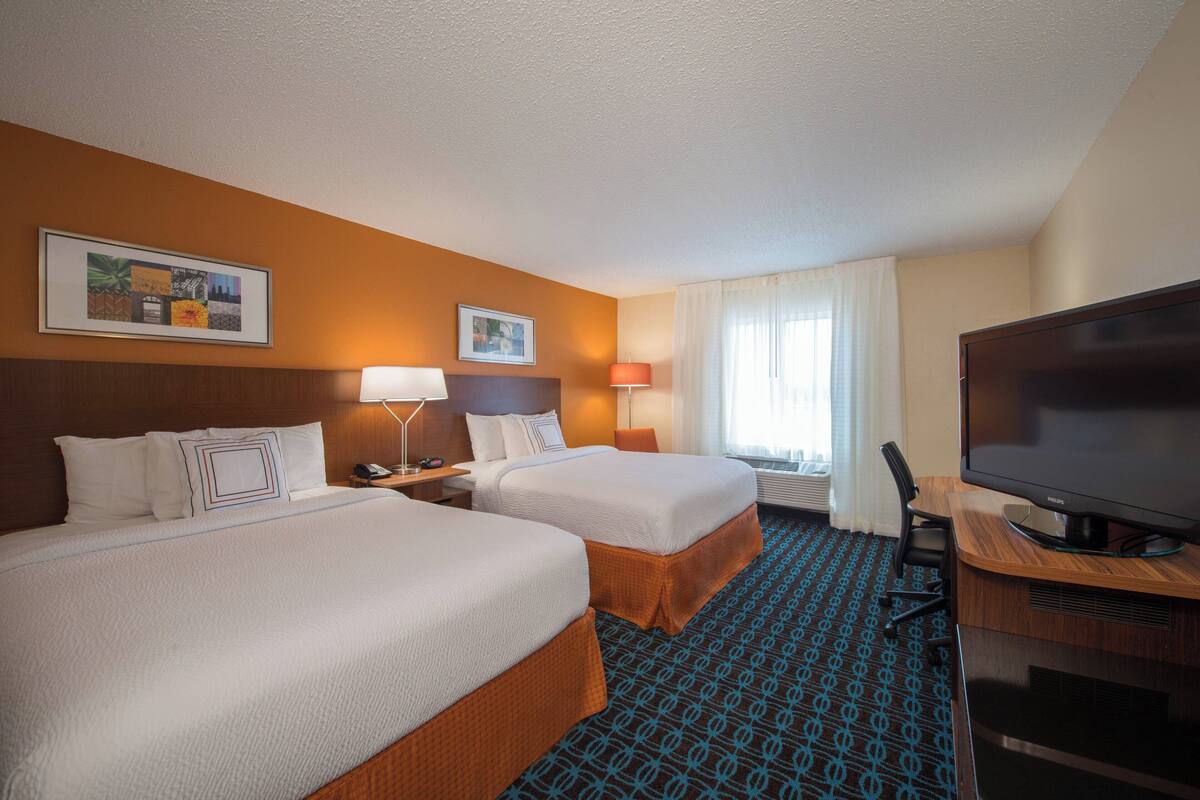 A hotel room with two beds, a desk with a flat-screen TV, a lamp, and a framed picture on the wall.