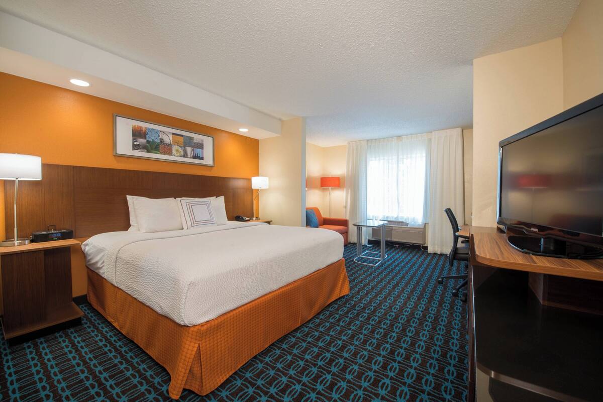 A hotel room with a large bed, a desk with a chair, a television, and a window with curtains.