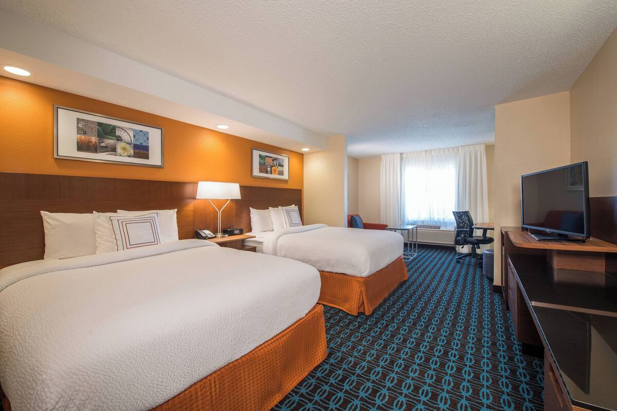 A hotel room with two beds, a desk, a television, and a window with curtains.