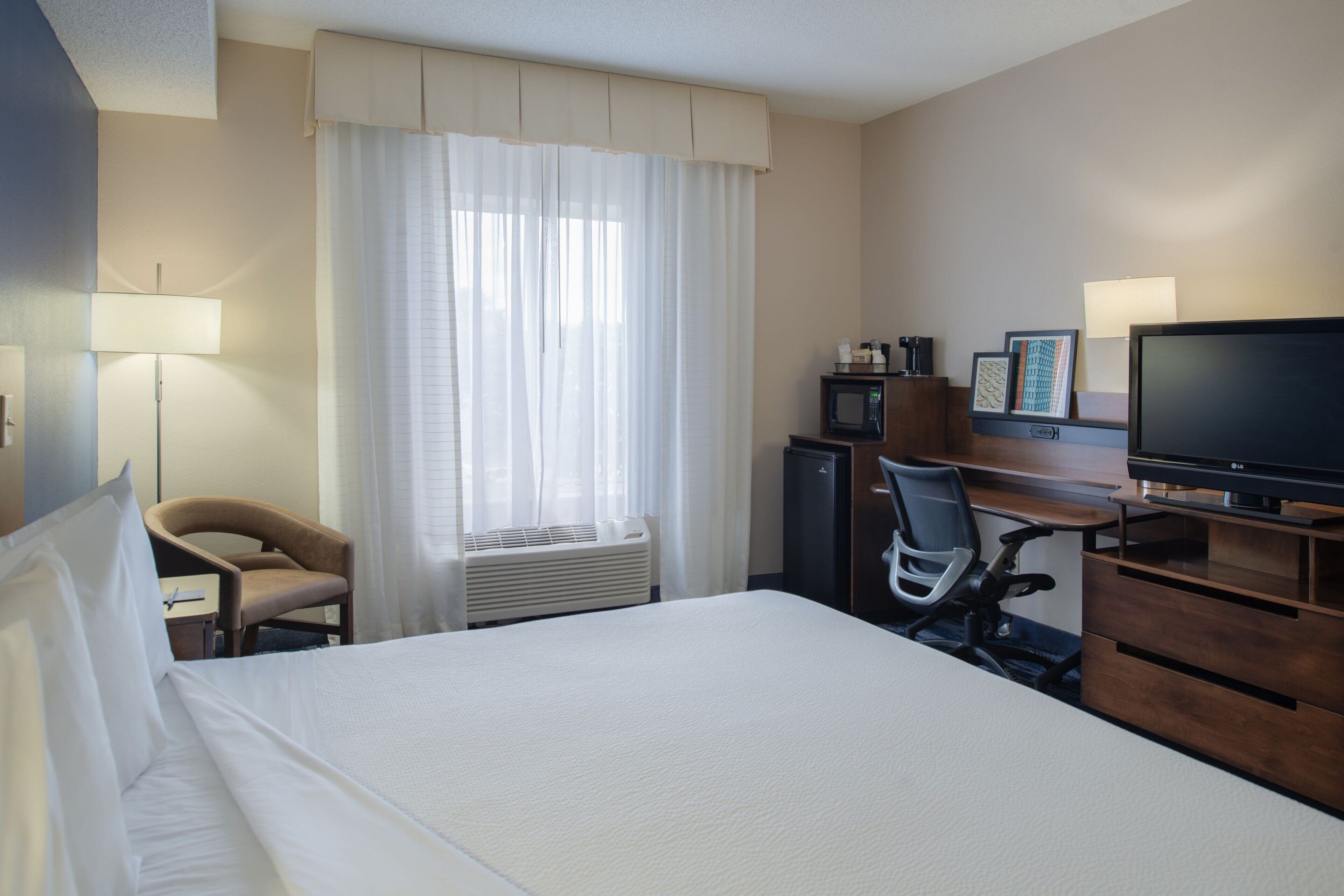 A hotel room with a large bed, a desk with a computer, a chair, a television, and a microwave.