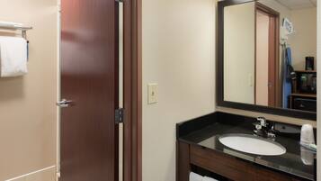 Une salle de bain d’hôtel avec une porte en bois, un lavabo blanc, un miroir et un porte-serviettes.