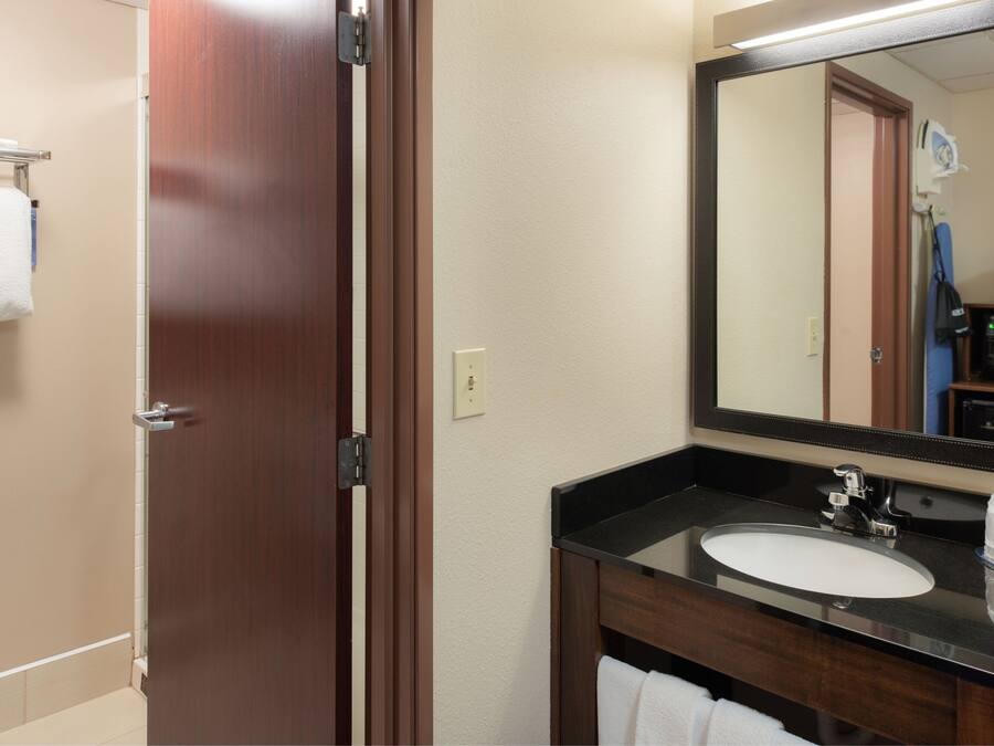 Une salle de bain d’hôtel avec une porte en bois, un lavabo blanc, un miroir et un porte-serviettes.