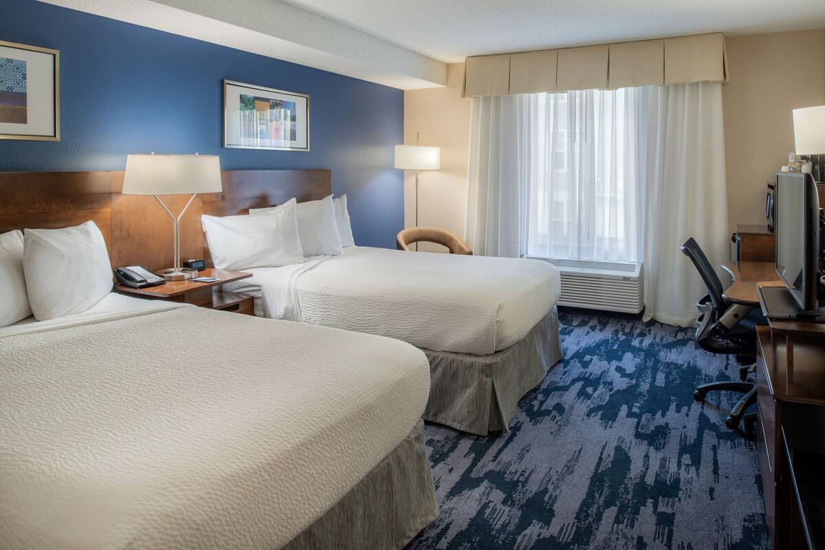A hotel room with two beds, a desk with a computer, a chair, and a TV.