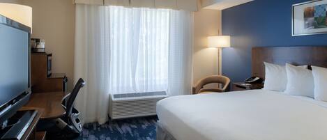 Une chambre d’hôtel avec un grand lit, un bureau doté d’un téléviseur à écran plat, une chaise, une lampe et une fenêtre avec des rideaux.