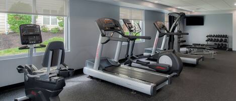 Un gimnasio con cintas de correr, elípticas y un soporte para pesas.