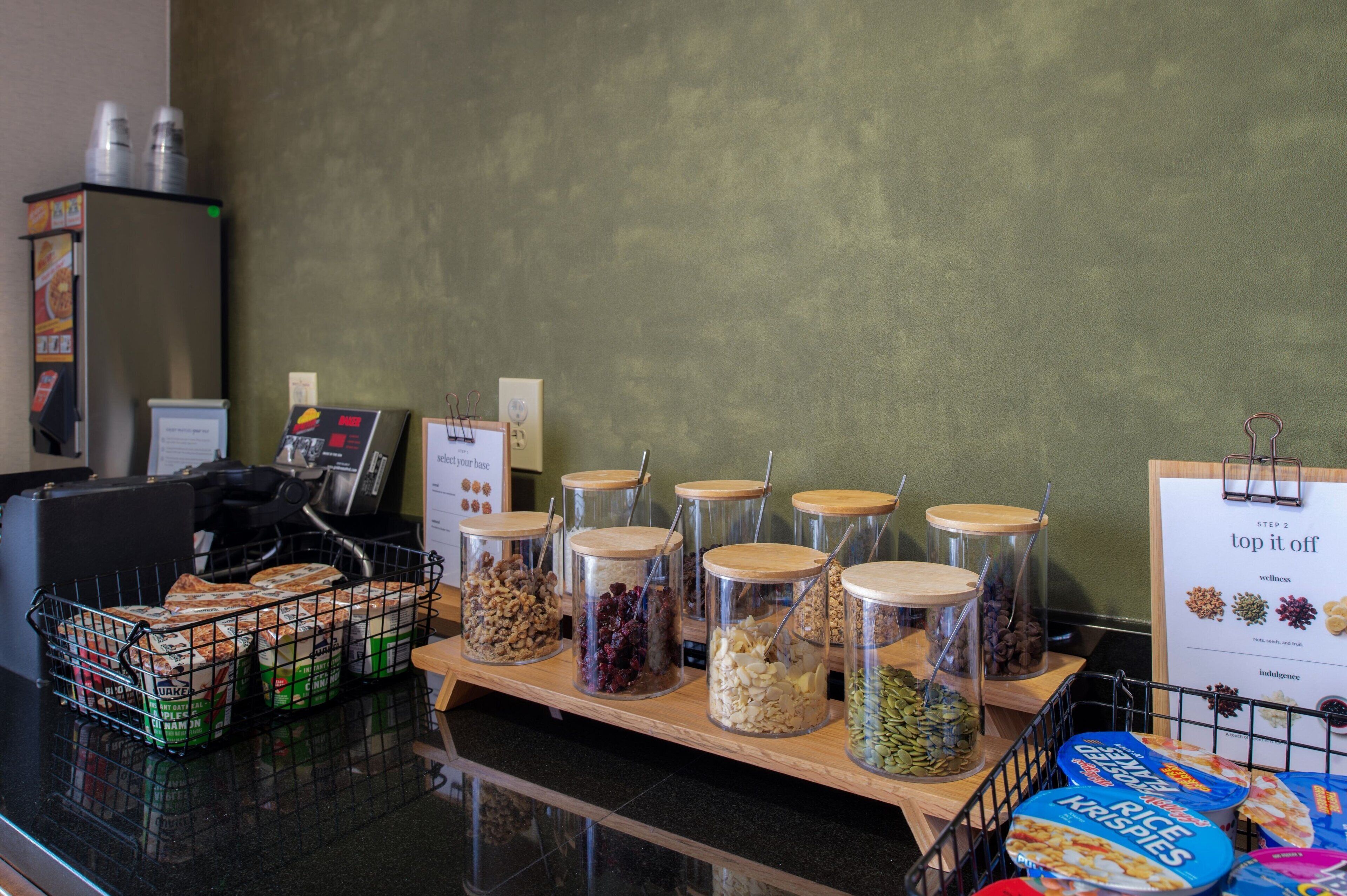 Un buffet où les clients peuvent se servir eux-mêmes pour le petit-déjeuner, avec différents choix d’aliments présentés dans des récipients en verre et des produits emballés.