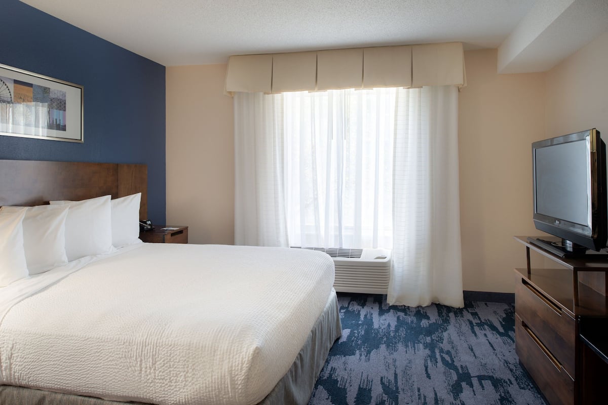 A hotel room with a large bed, a television, a nightstand, and a window with curtains.