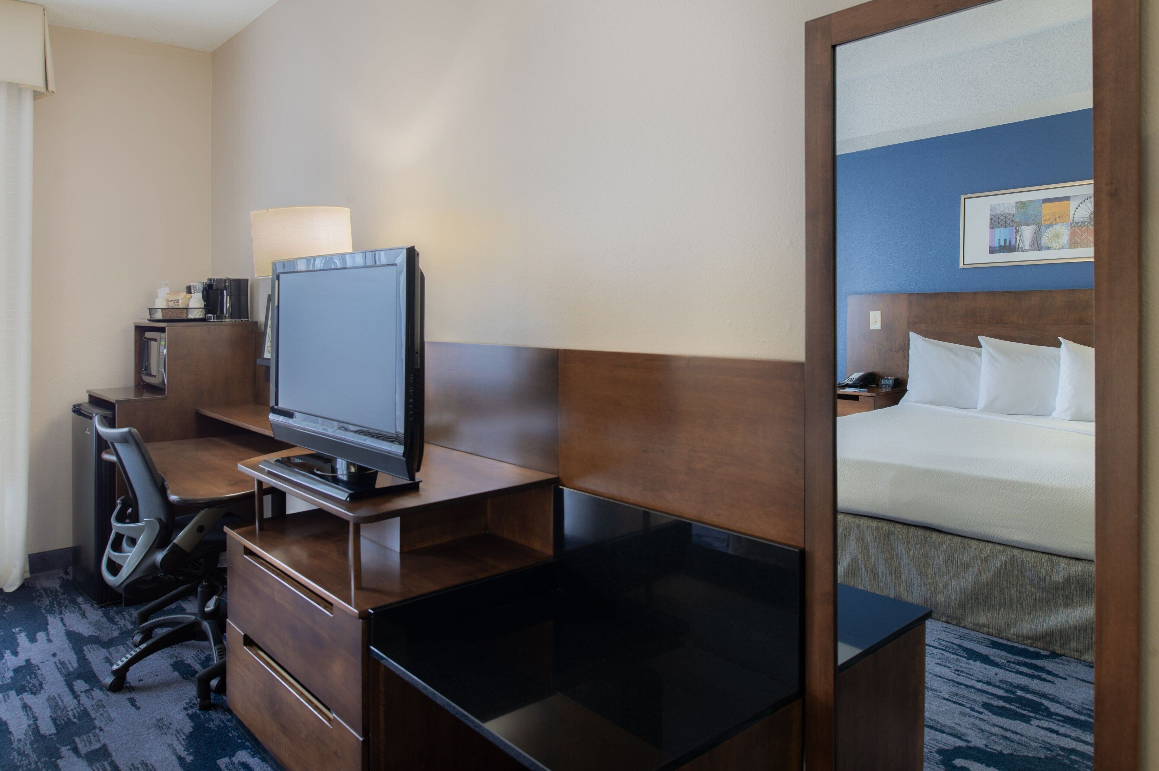 A hotel room with a bed, a desk with a computer, a chair, and a lamp.