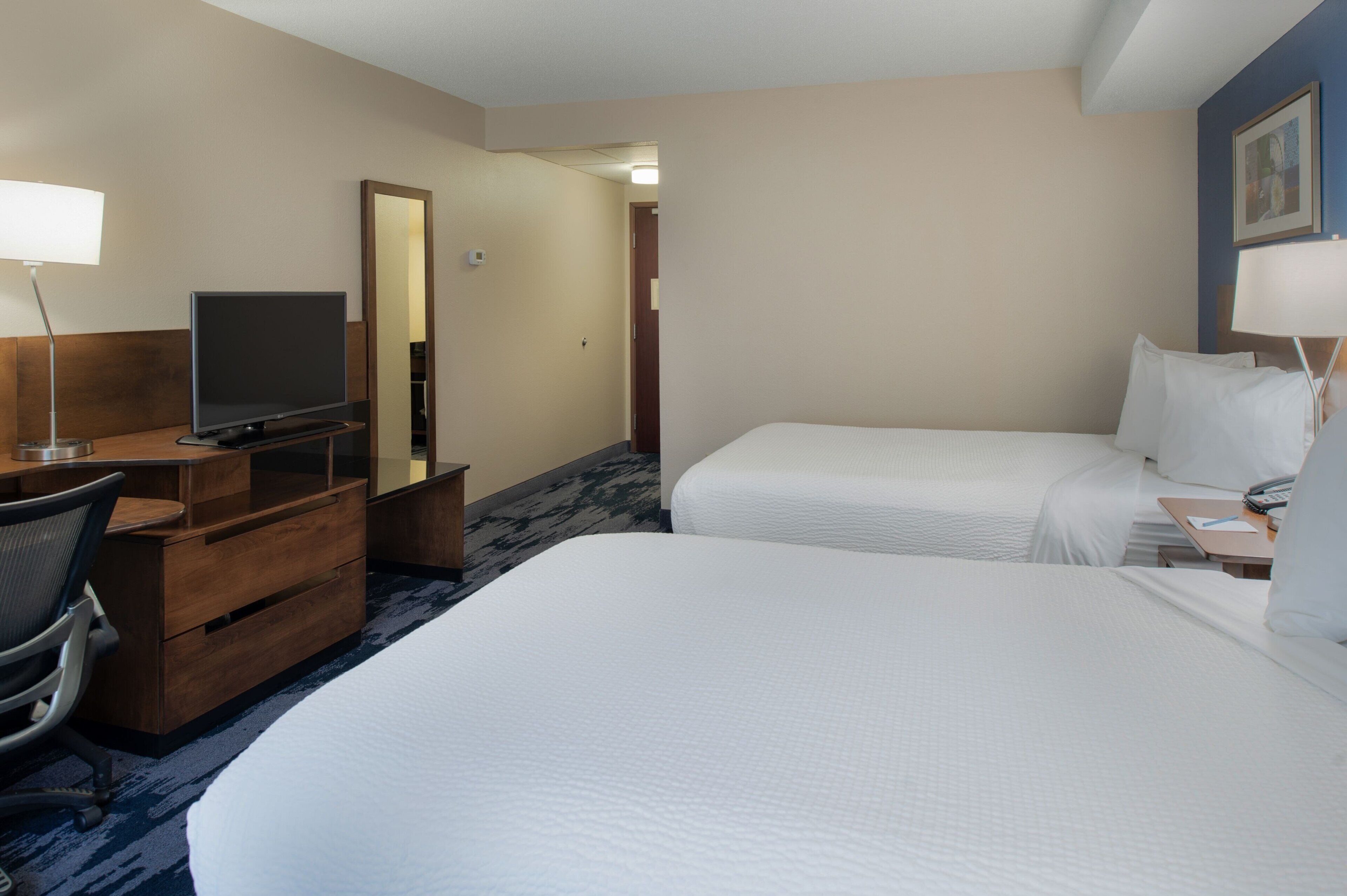 Una habitación de hotel con dos camas, un escritorio con televisor y un espejo.