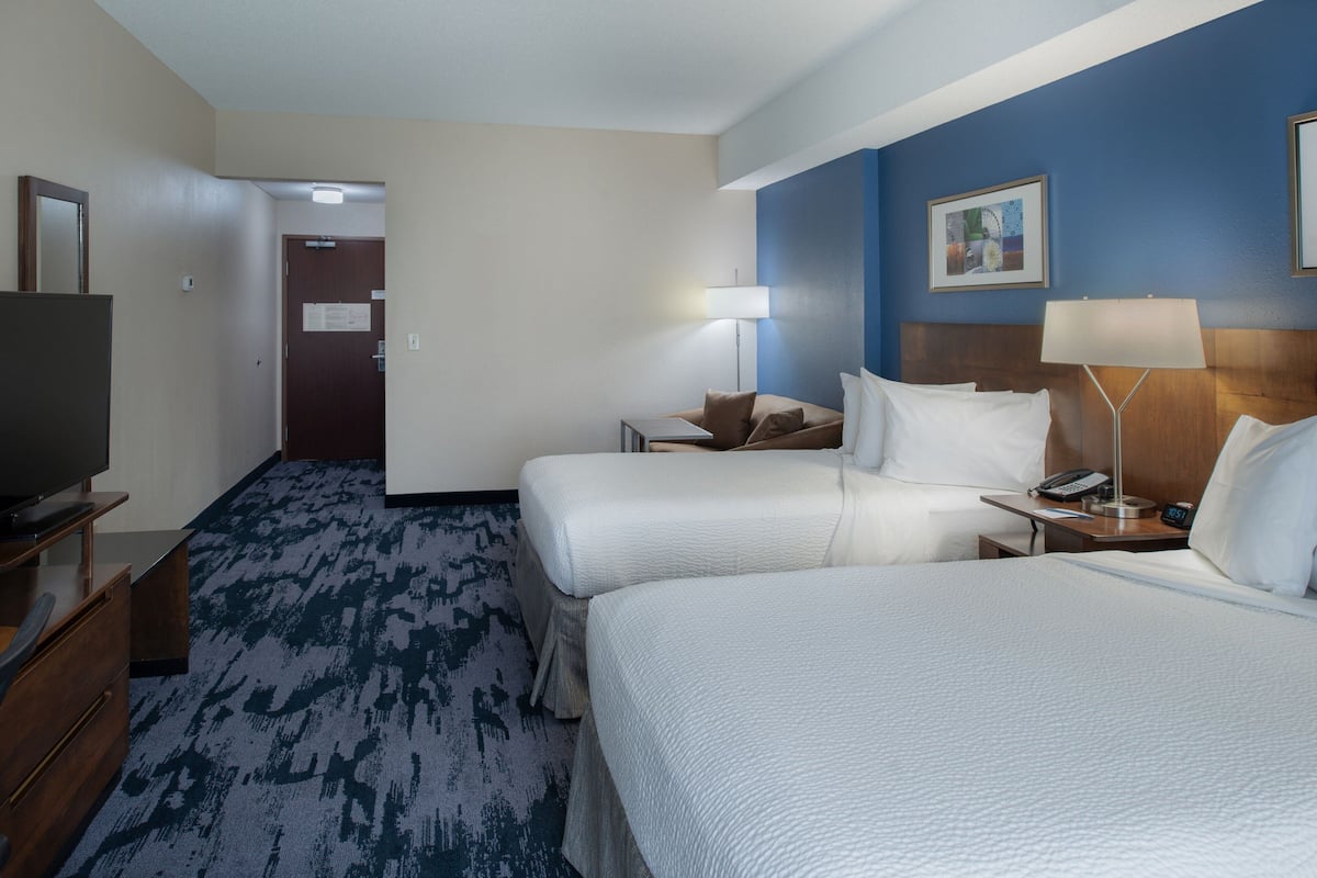 A hotel room with two beds, a television, a desk with a lamp, and a door leading to another room.