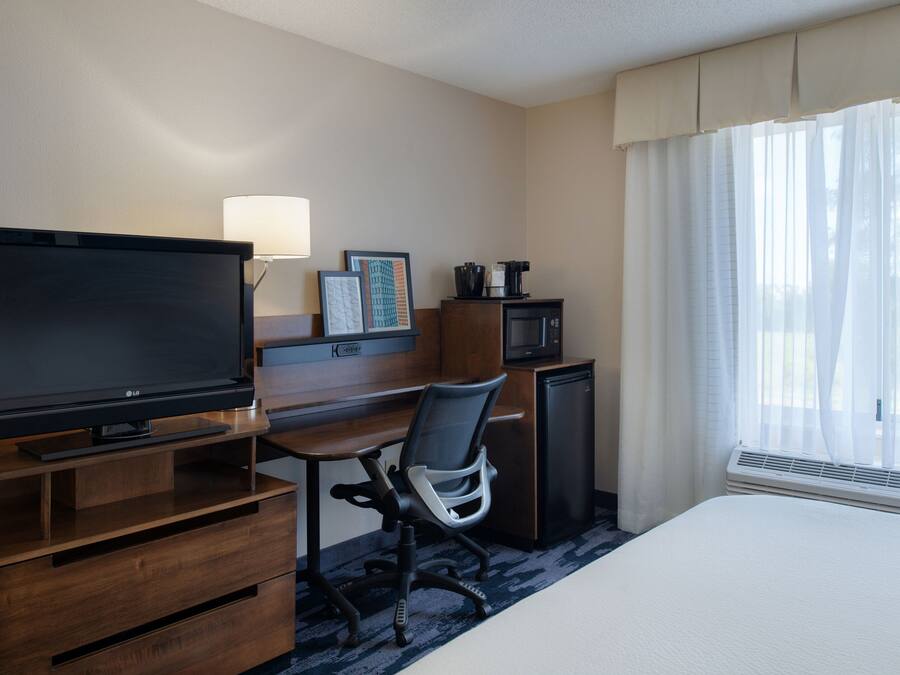 Una habitación de hotel con cama, televisor, escritorio con silla, microondas y ventana con cortinas.