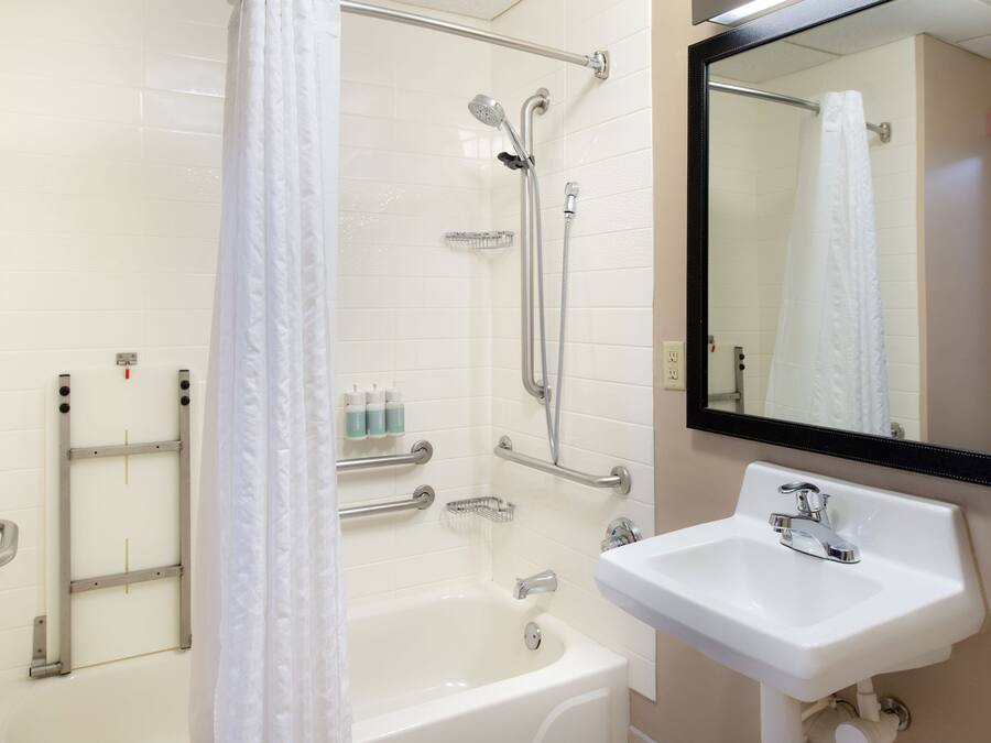 Un baño con bañera, ducha con cabezal de ducha manual, lavamanos y espejo.