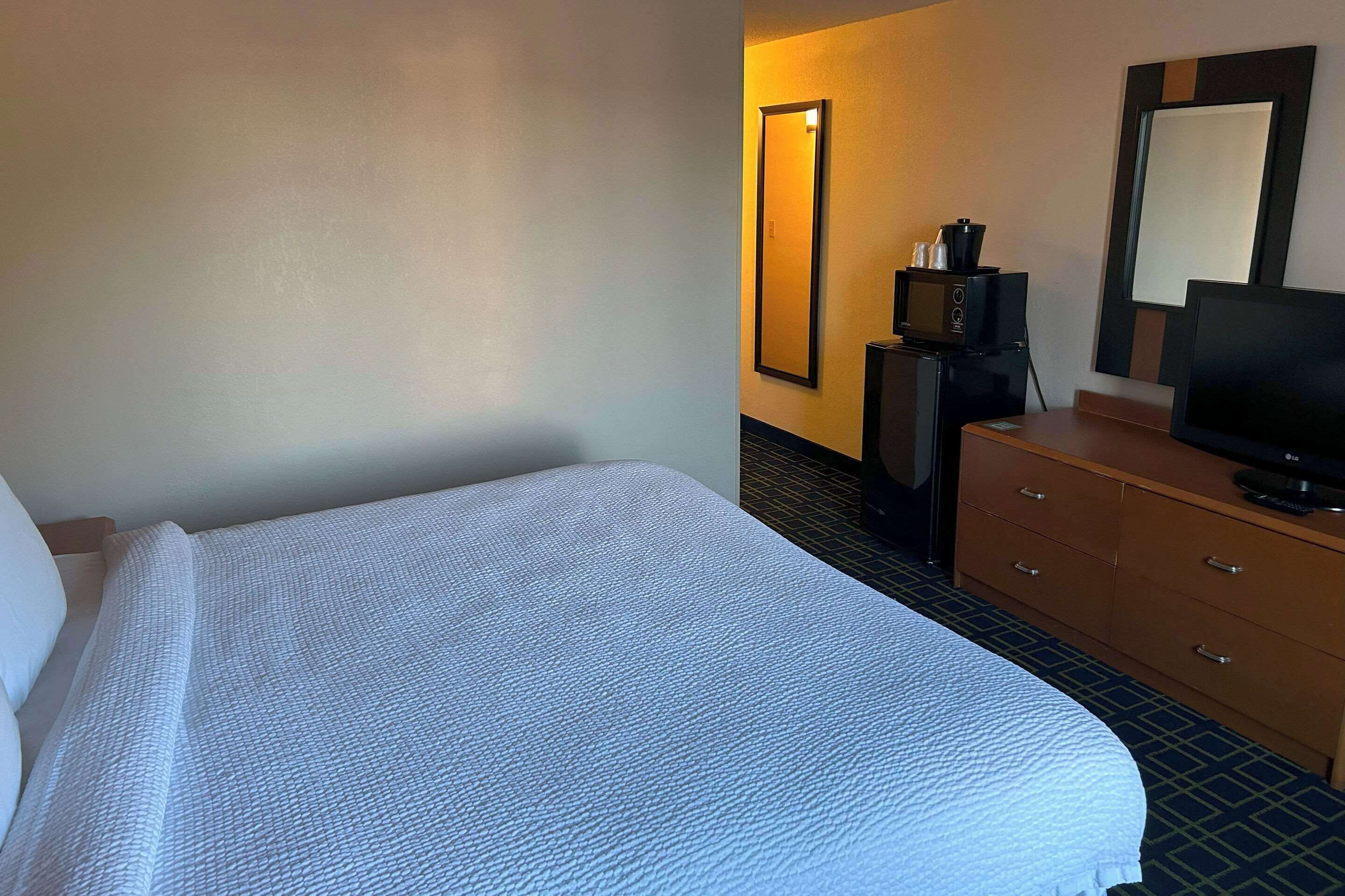 A hotel room with a bed, a television, a coffee maker, and a dresser.
